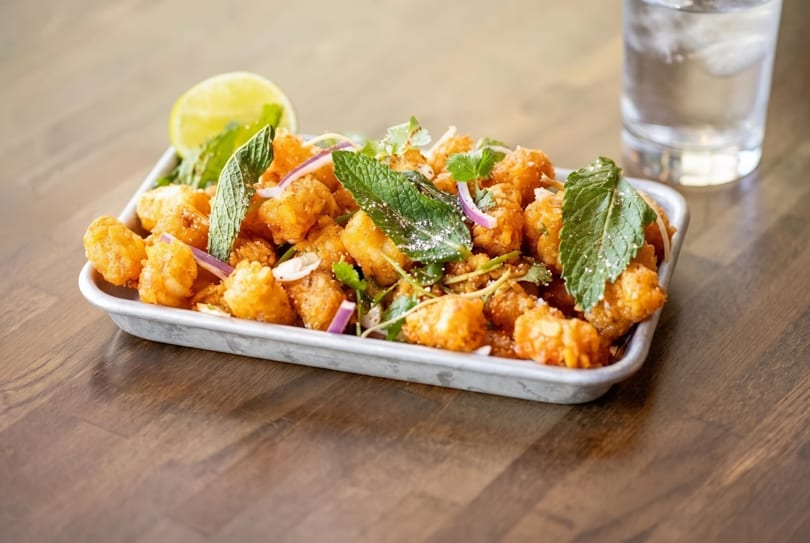 Crispy fried chicken bites with mint, cilantro, red onion, and lime on a metal tray.