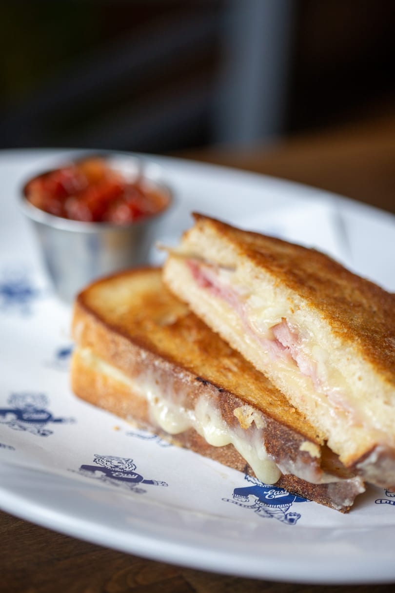 Grilled ham and cheese sandwich with melted cheese oozing out, served with a side of salsa.